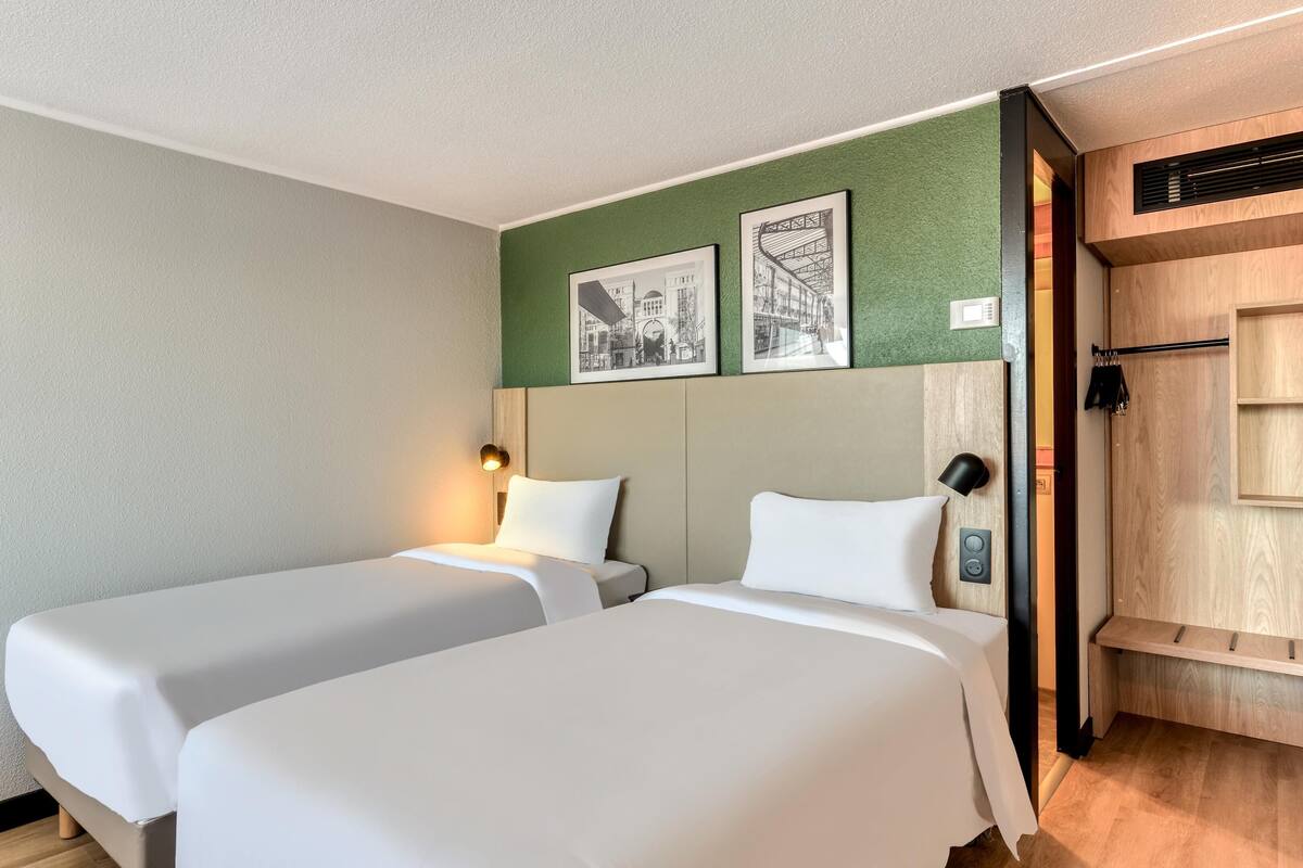 Een hotelkamer met twee bedden, een flatscreen televisie die aan de muur is bevestigd, en een groene accentmuur met ingelijste foto's.