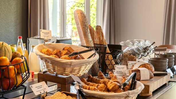 Un bufé de desayuno con panes, bollería y frutas variadas.
