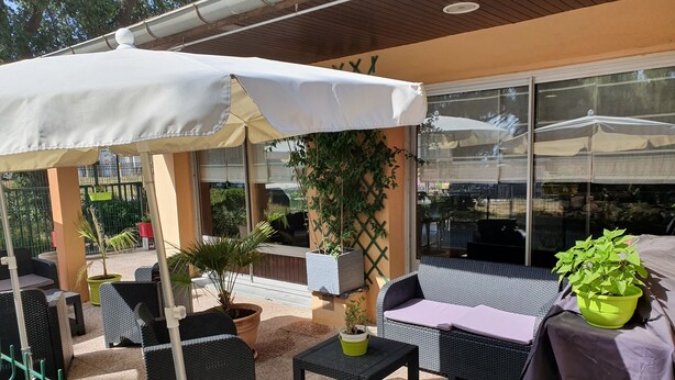 An outdoor patio area with wicker furniture, a covered seating area, and potted plants.
