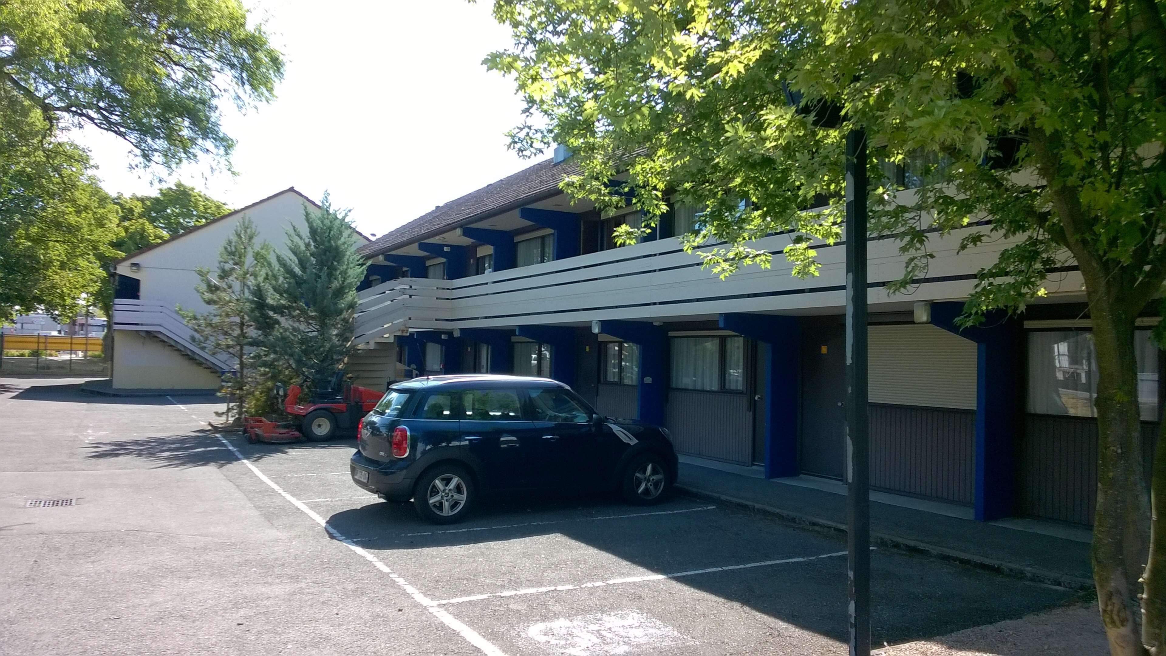 A parking lot with a blue car parked in front of a building with blue and white exterior walls.