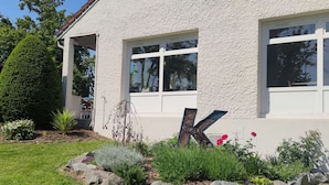 Un edificio blanco con ventanas grandes, un jardín bien cuidado con rocas y plantas, y una escultura prominente con la letra 'K' en primer plano.