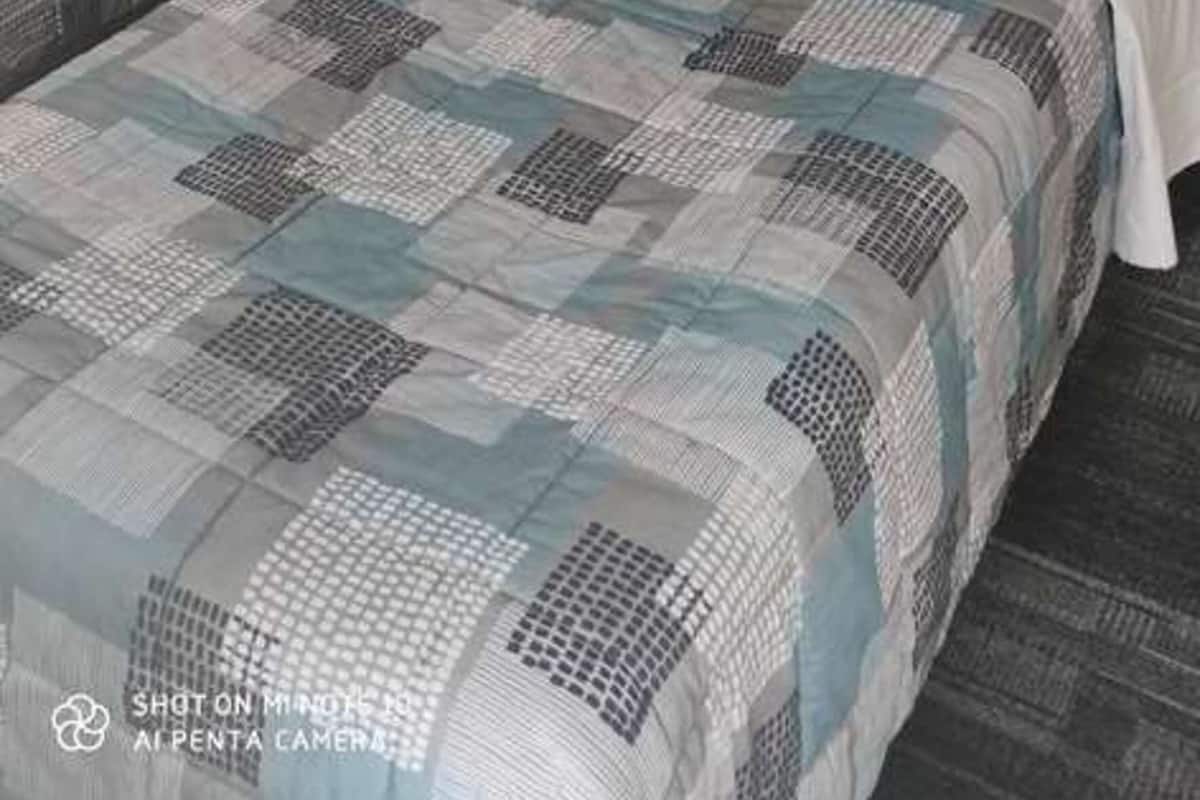 Habitación de hotel con dos camas individuales, cabecera de madera, pared azul y una mesita de noche con lámpara.