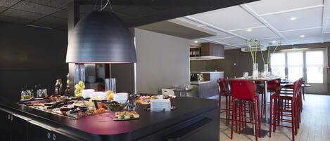 Una cocina moderna con una isla central, taburetes rojos y un comedor con mesa de vidrio.