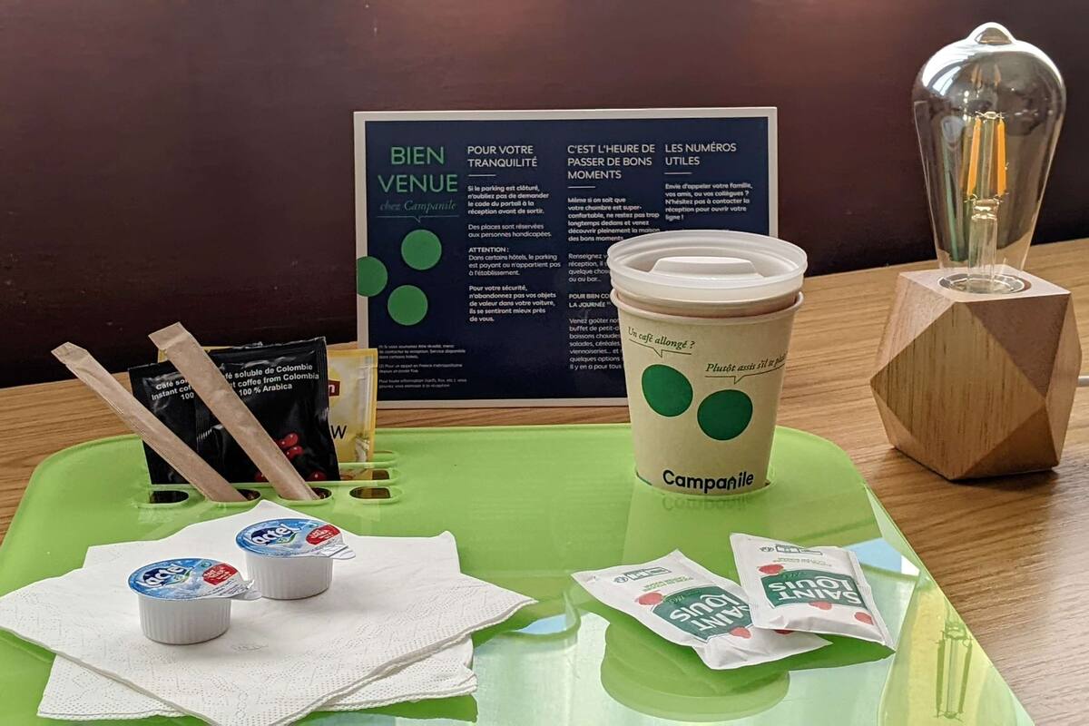 Una mesa con una bandeja verde, una taza de café, sobres de café instantáneo, una servilleta y un cartel con texto en francés.