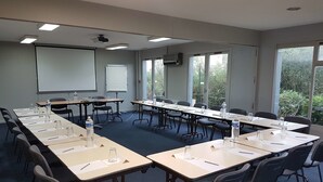 Ein Konferenzraum mit langen Tischen, Stühlen, einer Projektionsleinwand und großen Fenstern.