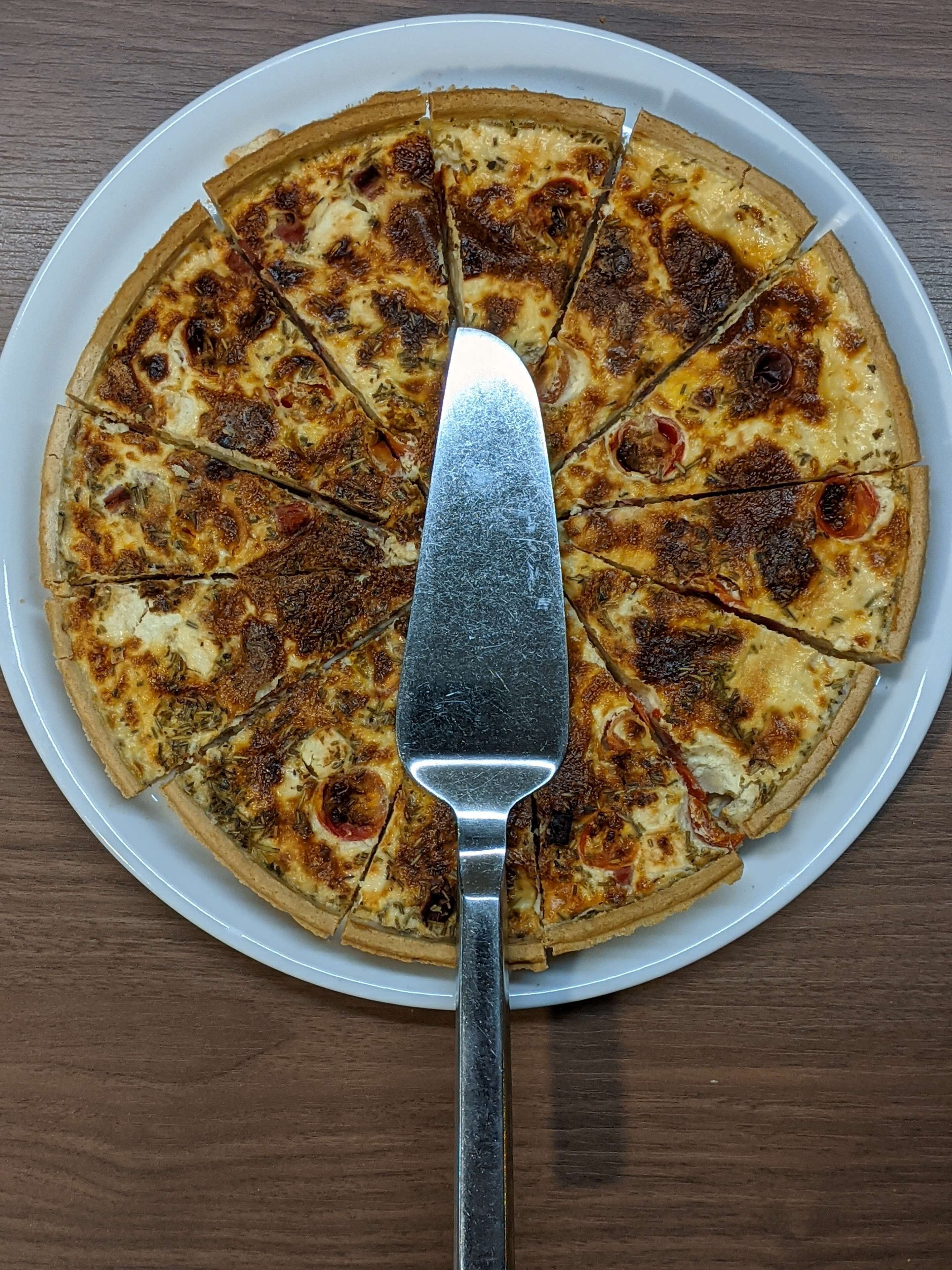 Eine Pizza auf einem weißen Teller, in der Mitte liegt ein Pizzaschneider.