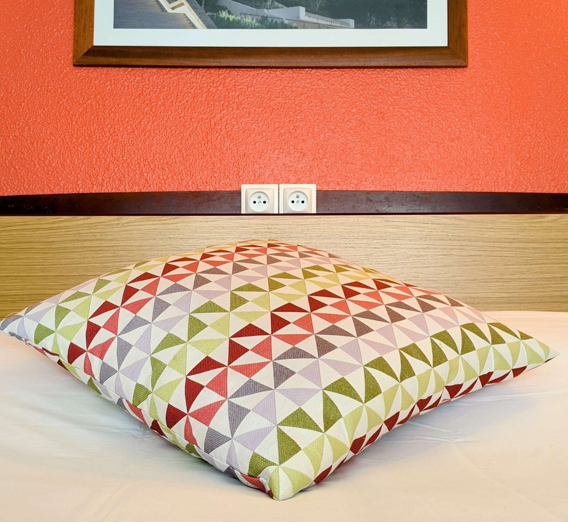 A bed with a patterned pillow, a wooden headboard, and a red wall with two electrical outlets.