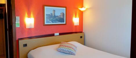 A hotel room with a bed, a framed picture on the wall, and two wall-mounted lights.