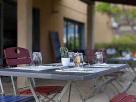 Un espace extérieur aménagé pour les repas, avec des tables et des chaises en métal, de la vaisselle transparente et un cactus.