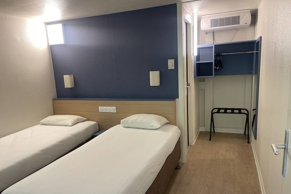 Ein Zimmer mit zwei Betten, einer Wand-Klimaanlage und einem kleinen Stuhl.