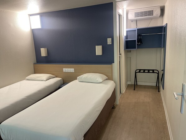 A room with two beds, a wall-mounted air conditioner, and a small chair.