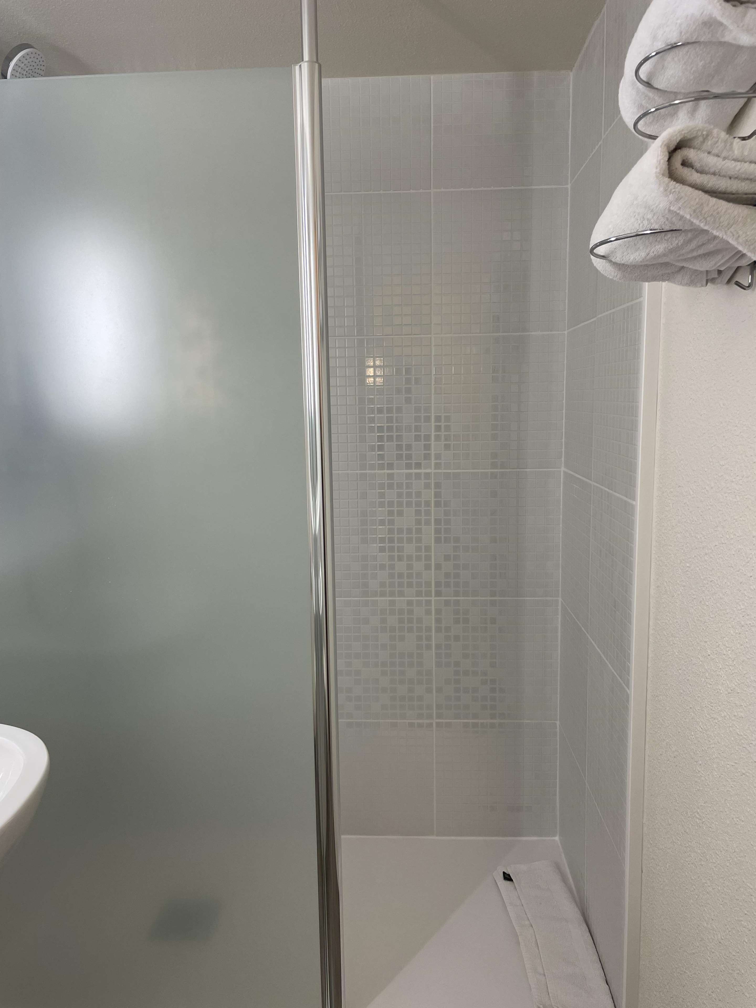 Un baño con cabina de ducha de vidrio, paredes con azulejos y un perchero.