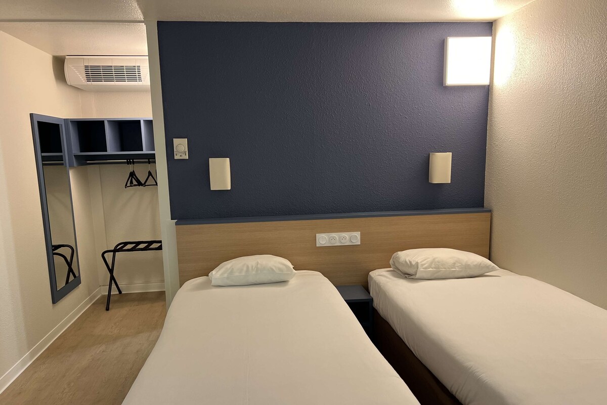 Ein Hotelzimmer mit zwei Einzelbetten, einem Schrank, einem Spiegel und einer Wandklimaanlage.