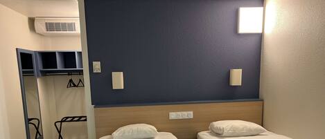 Habitación de hotel con dos camas individuales, un armario, un espejo y un aire acondicionado instalado en la pared.