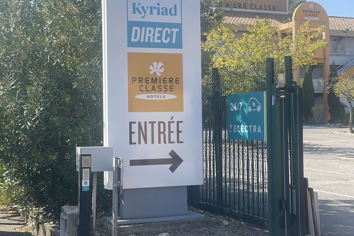 Ein Schild am Eingang eines Hotels, 'Kyriad Direct', mit einem Pfeil, der den Eingang weist.