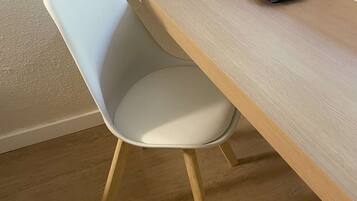 Une chaise moderne avec un siège blanc et des pieds en bois, placée devant un bureau en bois sur lequel se trouvent une bouilloire et des tasses.