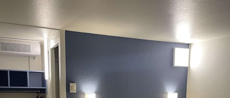 A hotel room with two single beds, a small table, and a wall-mounted shelf.