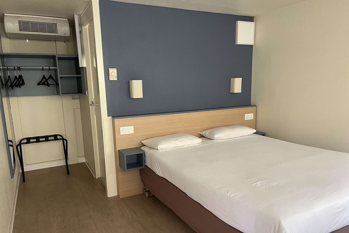 Ein Hotelzimmer mit Bett, Nachttisch, Kleiderschrank und einer Garderobe.