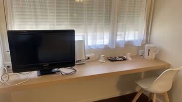 Un escritorio de madera con un monitor negro, una silla blanca, una tetera blanca y una bandeja con tazas y una caja pequeña.