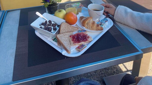 Een tafel met een dienblad waarop ontbijtartikelen liggen, zoals toast, jam, een croissant en een kop koffie.