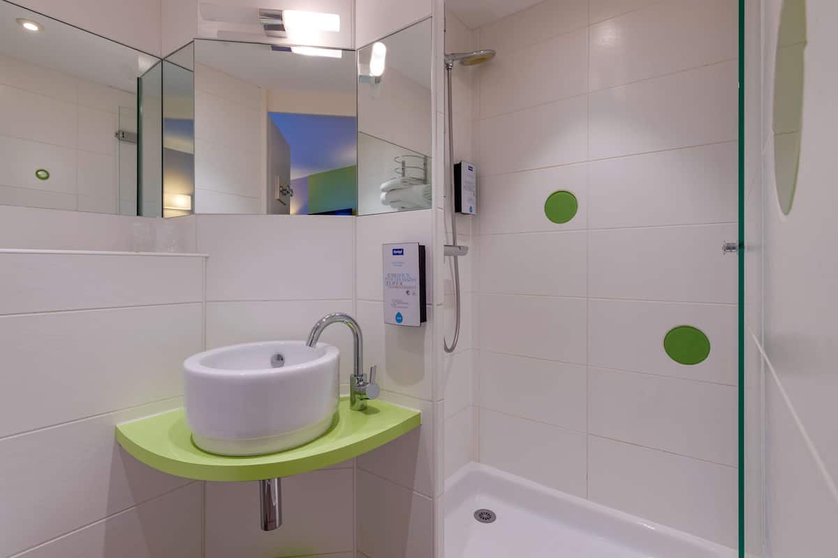 Ein Badezimmer mit Waschbecken in Weiß, einer grünen Arbeitsplatte und einer Duschkabine.