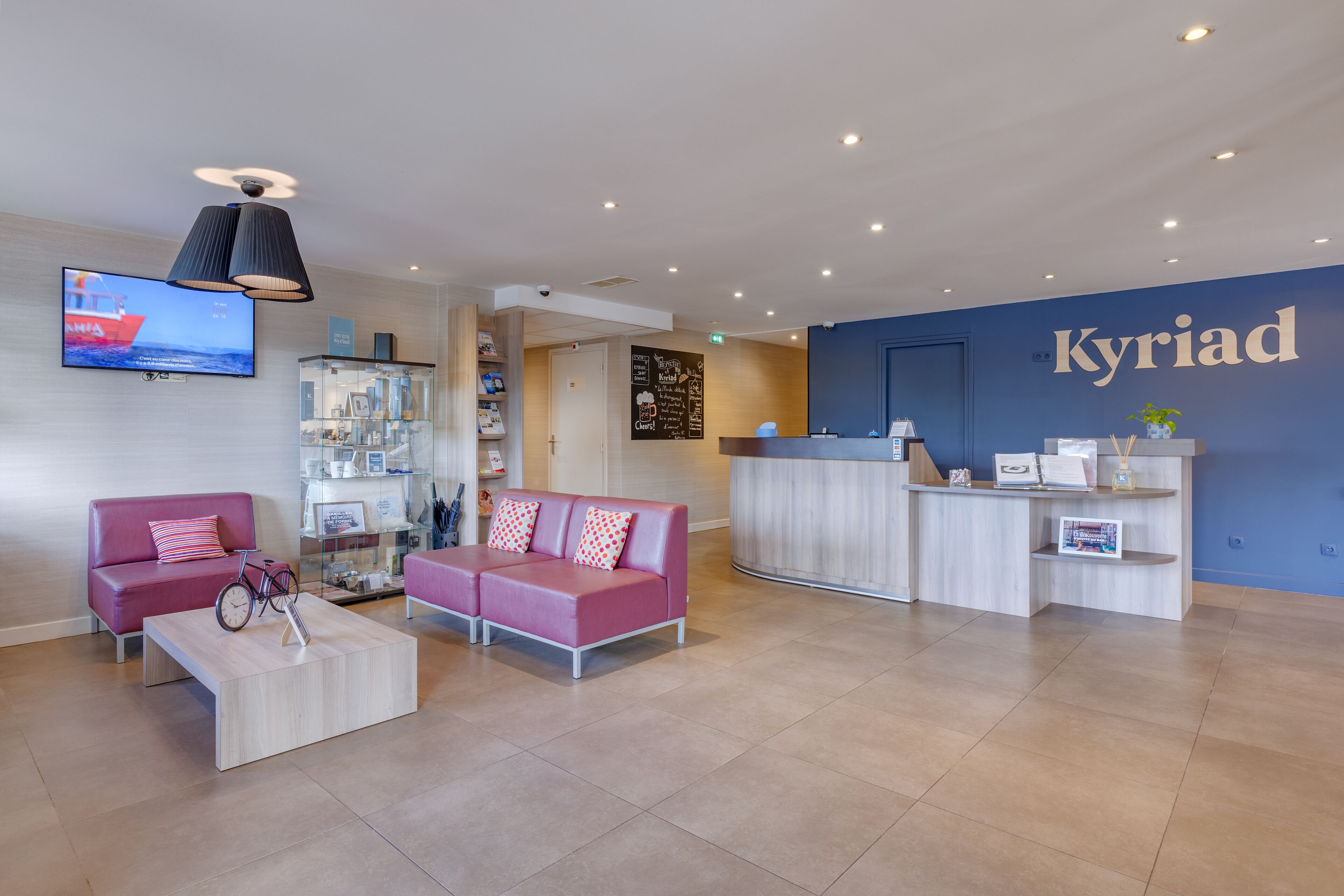 A reception area with a blue wall, a reception desk, two pink sofas, a coffee table, and a TV displaying a ship.