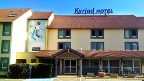 A hotel with a red-tiled roof, a sign reading "Kyriad Hotel," and a large mural on the side. - Hôtel Kyriad Lyon Est (Saint-Bonnet-de-Mure)