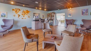 A modern lobby with a world map, seating area, bar, and a coffee machine. - Hôtel Kyriad Lyon Est (Saint-Bonnet-de-Mure)