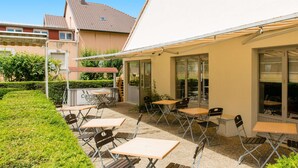 An outdoor patio area with tables and chairs, a covered seating area, and a view of the adjacent building. - Hotel Campanile Mulhouse Sud - Morschwiller (Morschwiller-le-Bas)