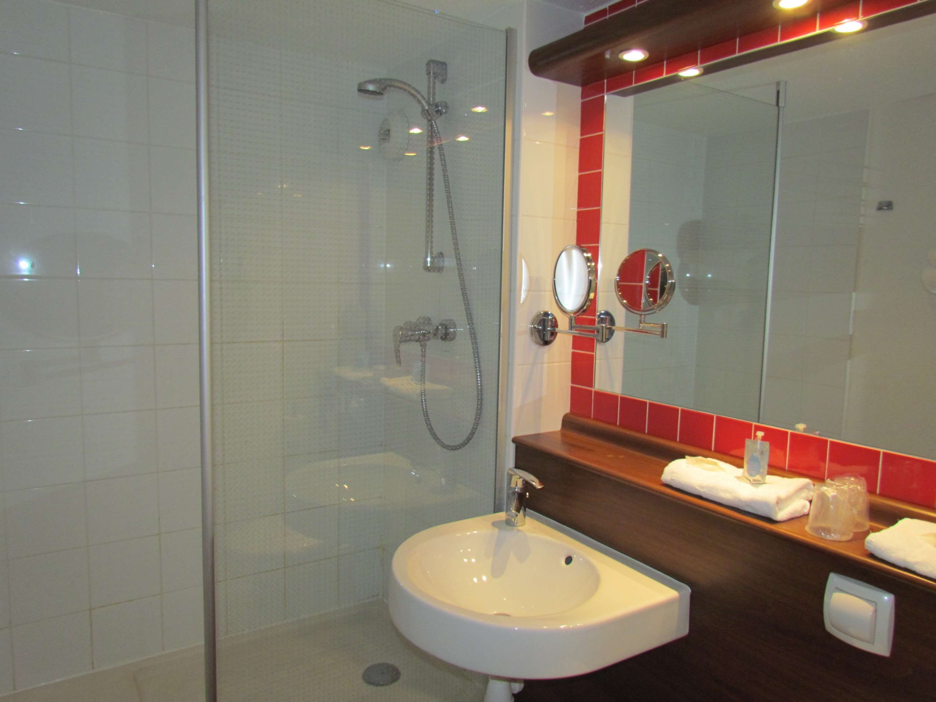 A bathroom with a glass-enclosed shower, a white sink, and a mirror with red-tiled backsplash.