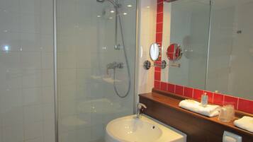 A bathroom with a glass-enclosed shower, a white sink, and a mirror with red-tiled backsplash.