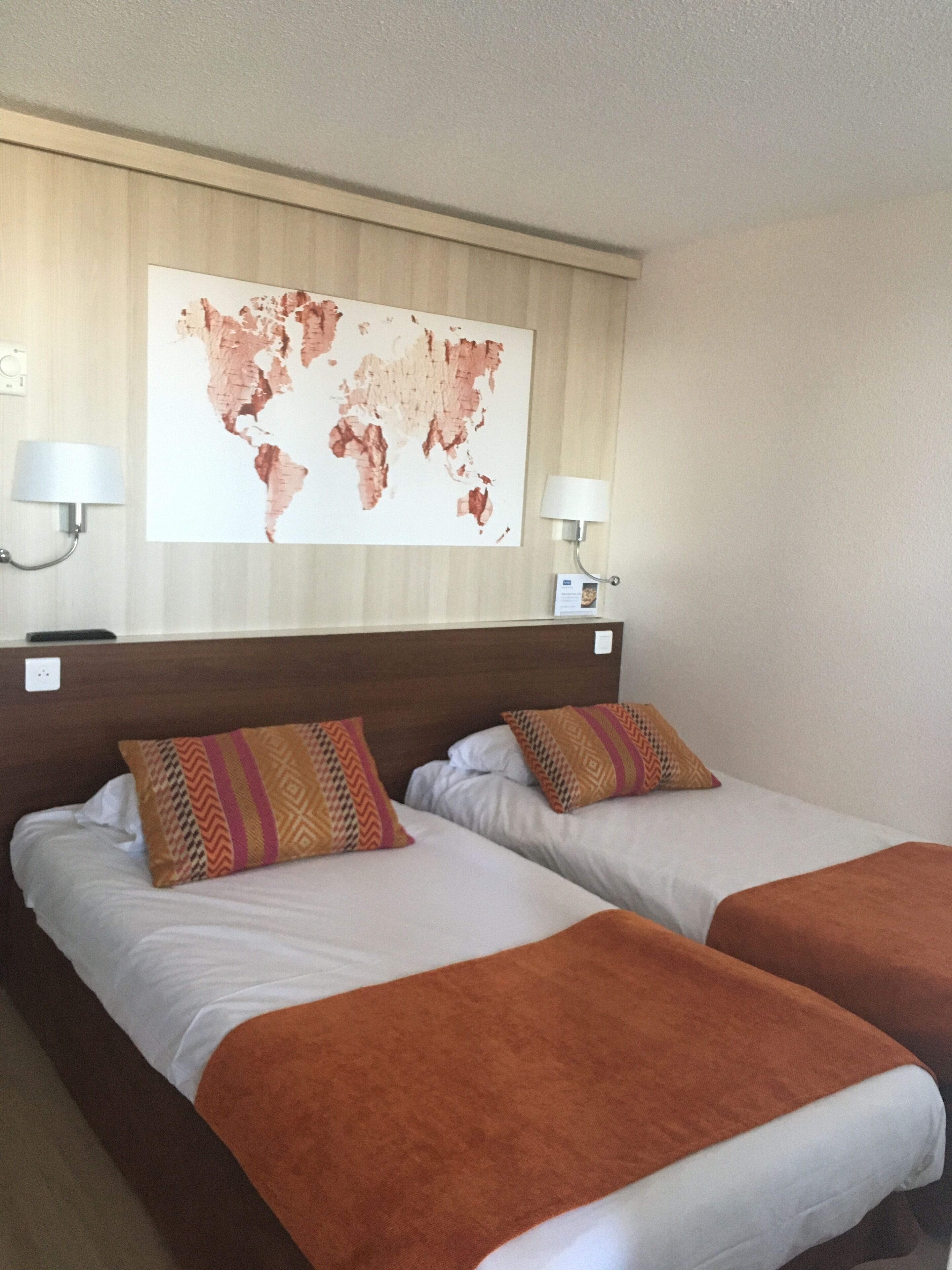 A hotel room with two beds, a world map on the wall, and two bedside lamps.
