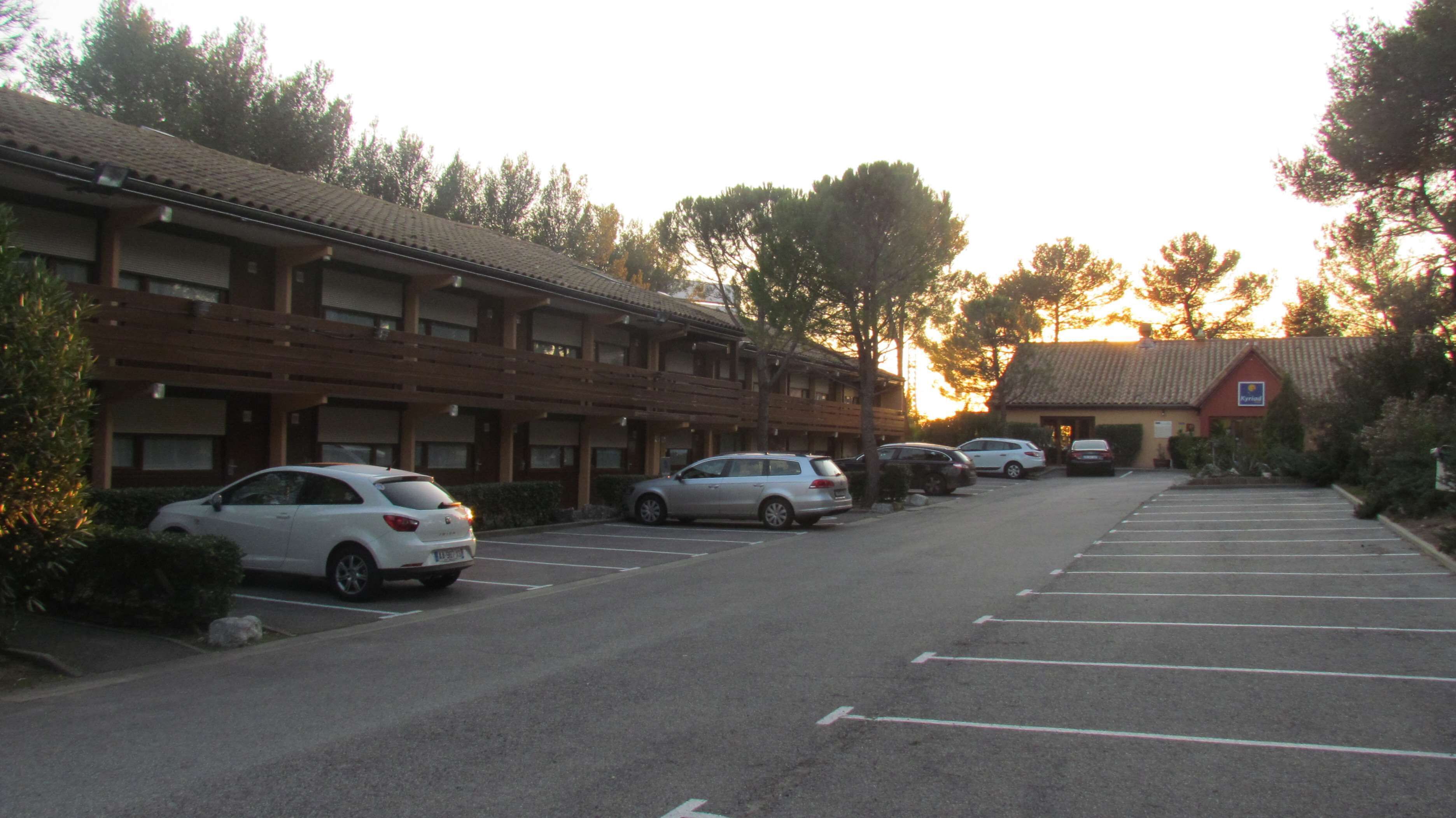 Una fila de espacios de estacionamiento frente a un hotel, con un edificio rojo al fondo.