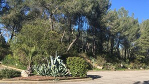 A parking lot with a row of trees and a small garden area with various plants. - Kyriad Montpellier NORD - Parc Euromédecine (Saint-Clement-de-Riviere)