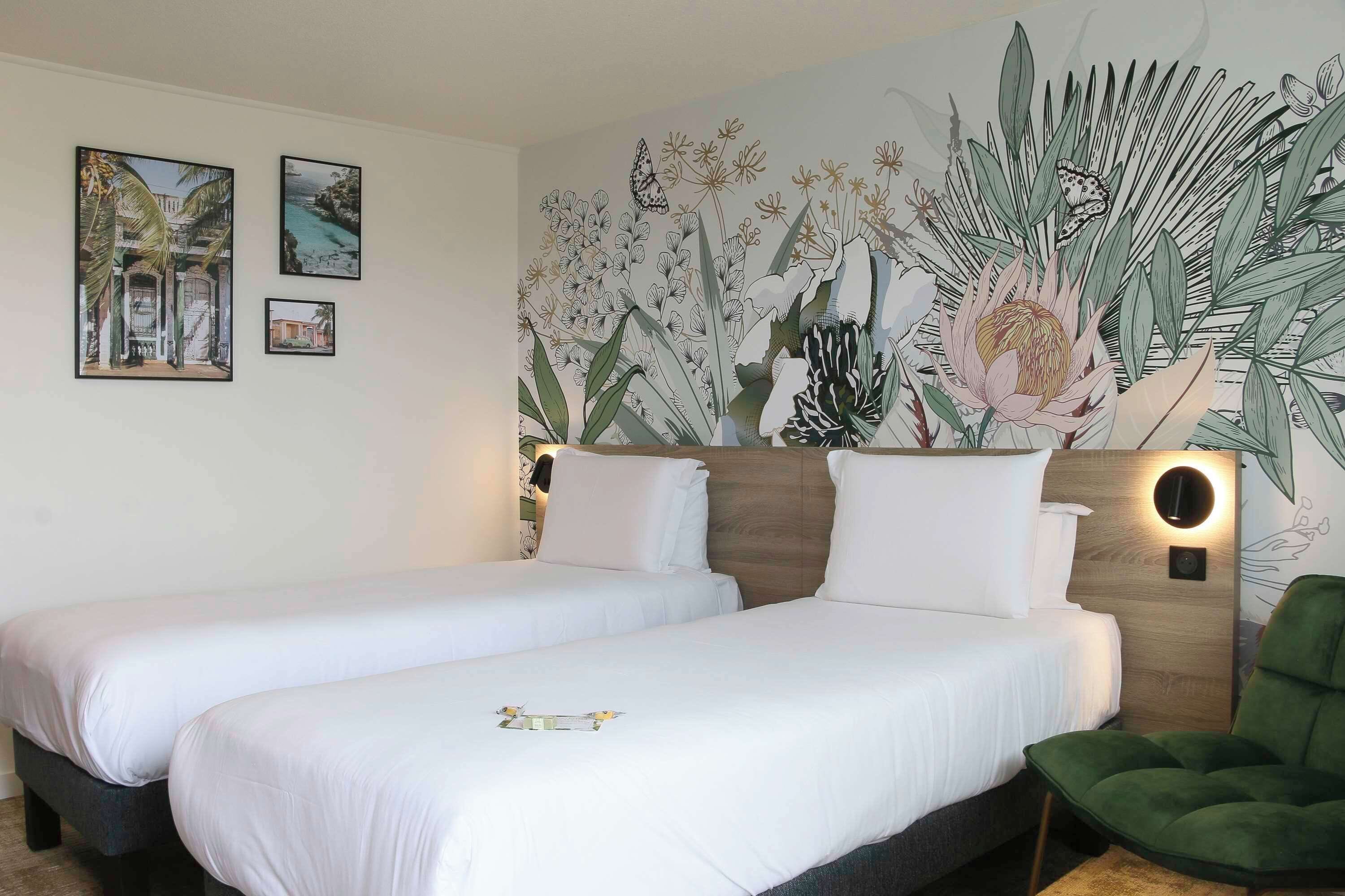Habitación de hotel con dos camas, una silla verde y un mural de plantas tropicales y mariposas.