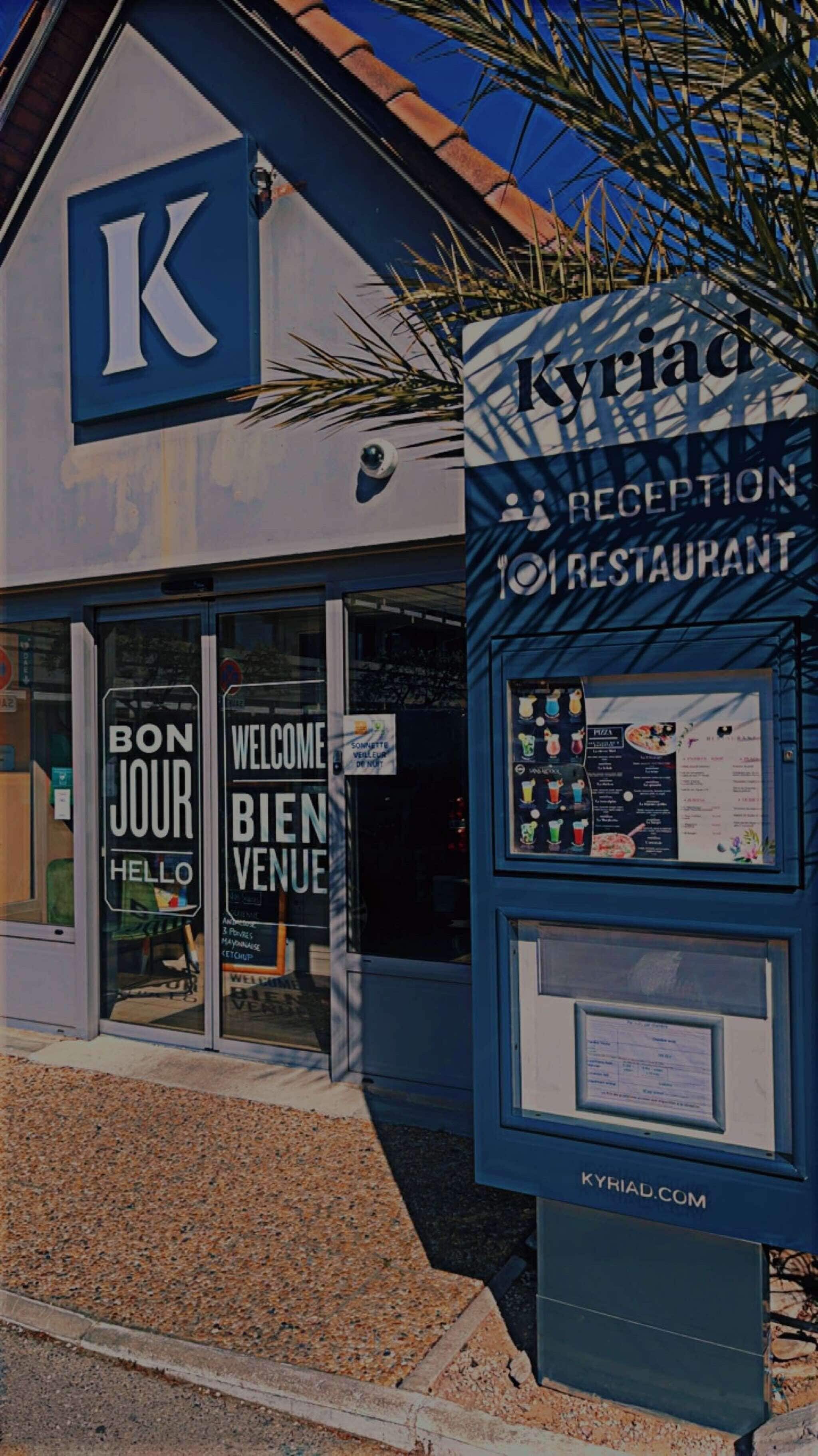 Un edificio con un gran letrero 'K', una zona de recepción y un tablero de menú.
