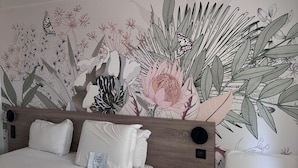 Habitació d'hotel amb dos llits, un panell de fusta al capçal i un mural floral a la paret.
