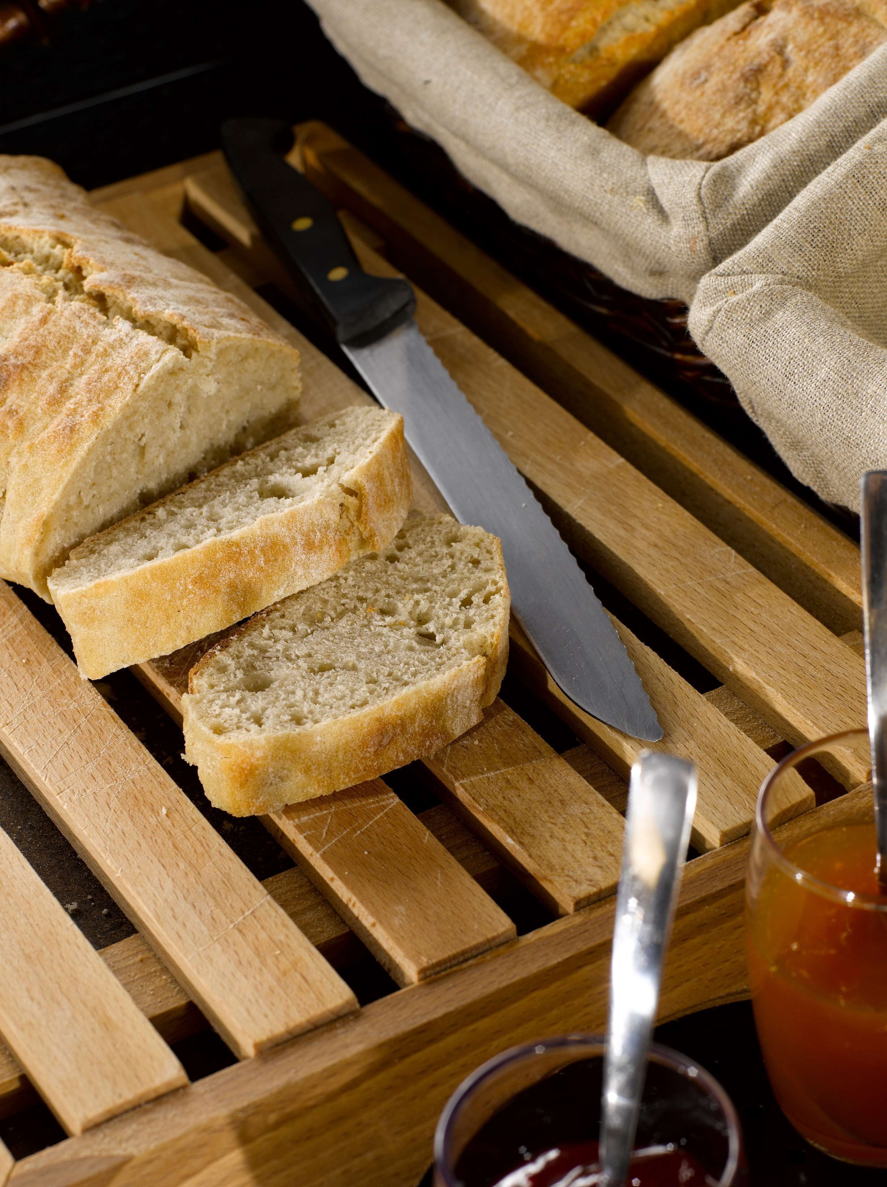 Brotscheiben auf einem Holzschneidebrett mit einem Messer und einem Marmeladenglas.