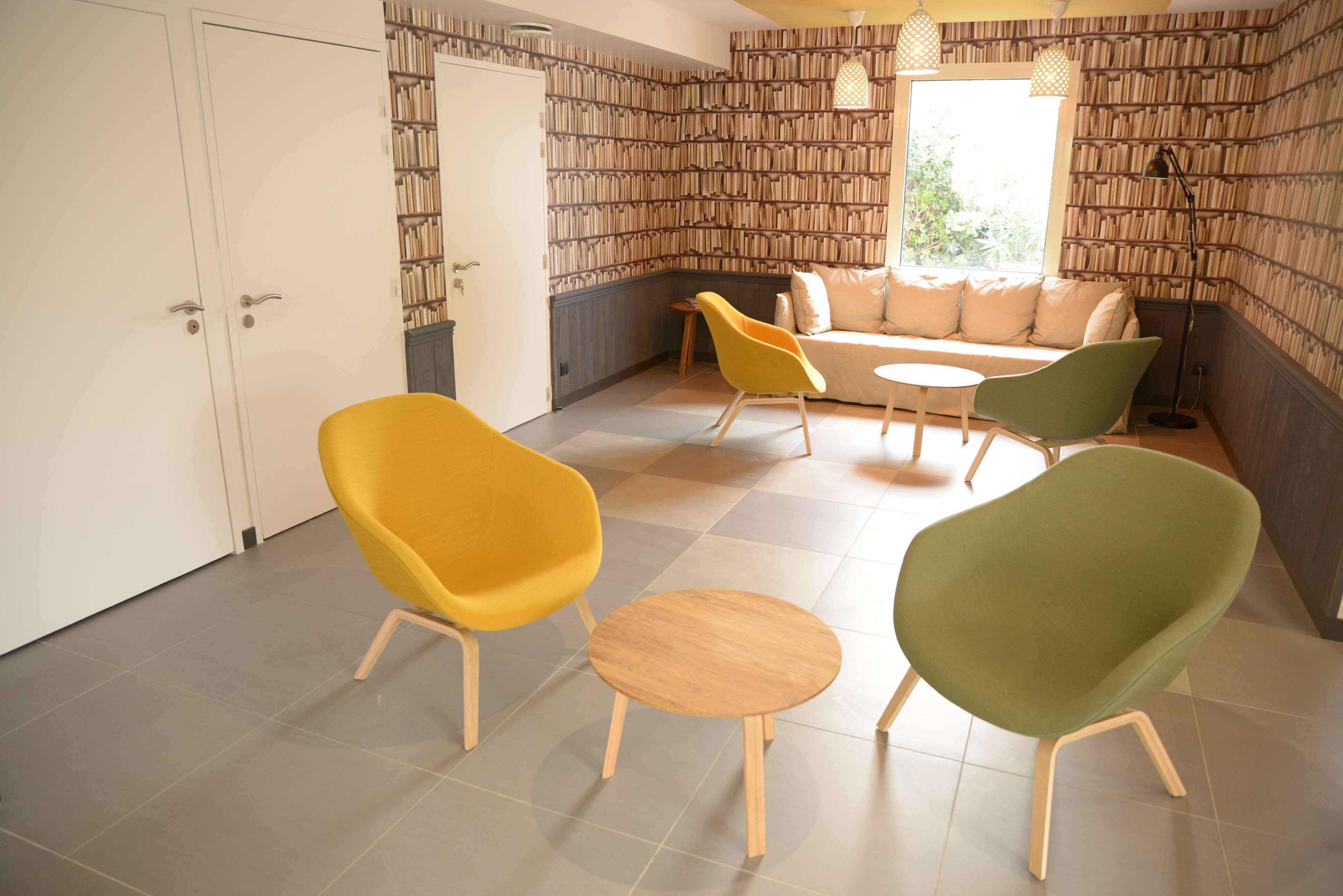 A room with a sofa, two chairs, a small table, and a bookshelf wall.