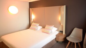 Une chambre d’hôtel moderne avec un grand lit, deux lampes de chevet et un fauteuil.