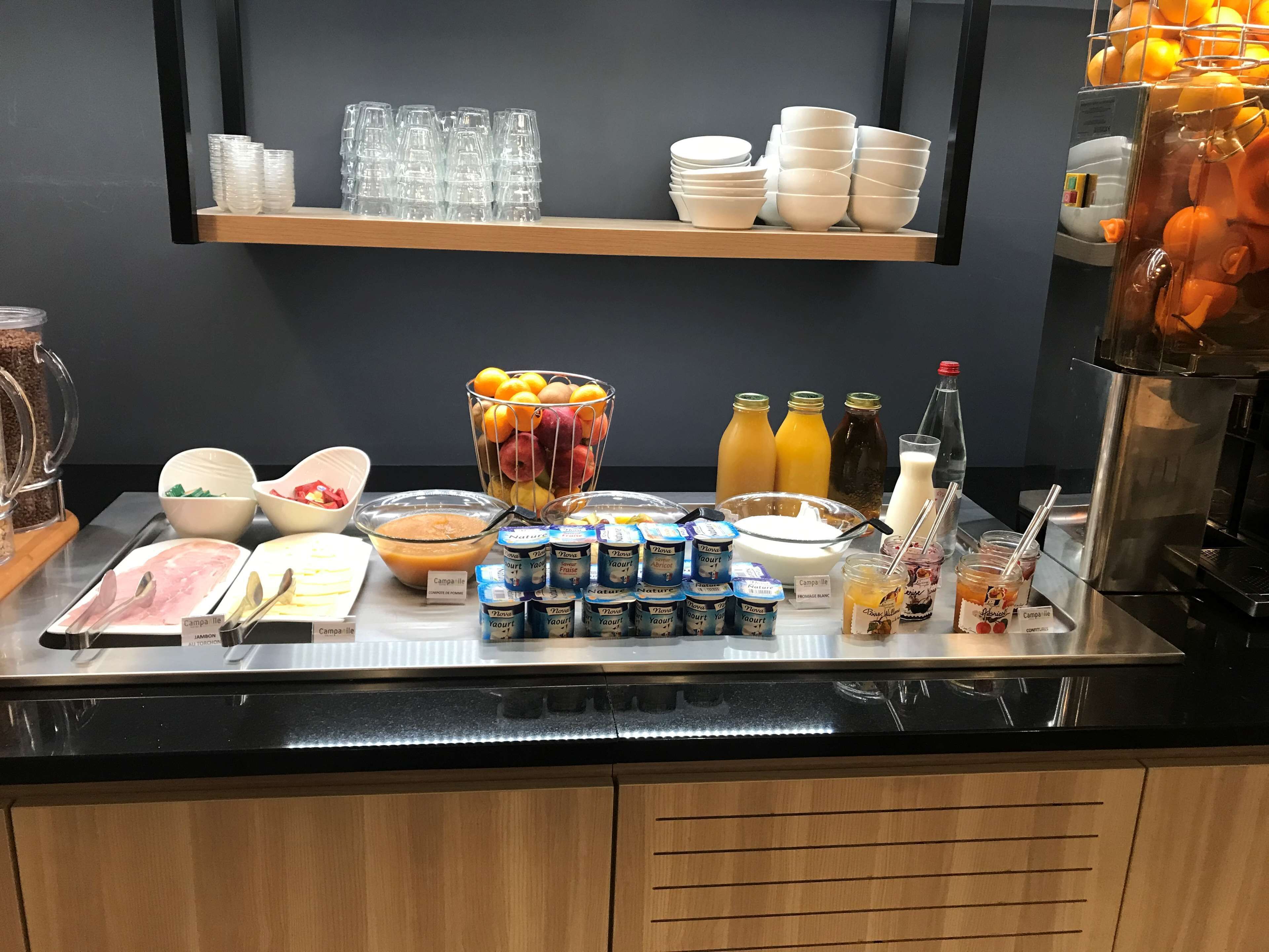 A buffet setup with various food items and beverages, including bowls of fruit, cartons of yogurt, and bottles of juice.