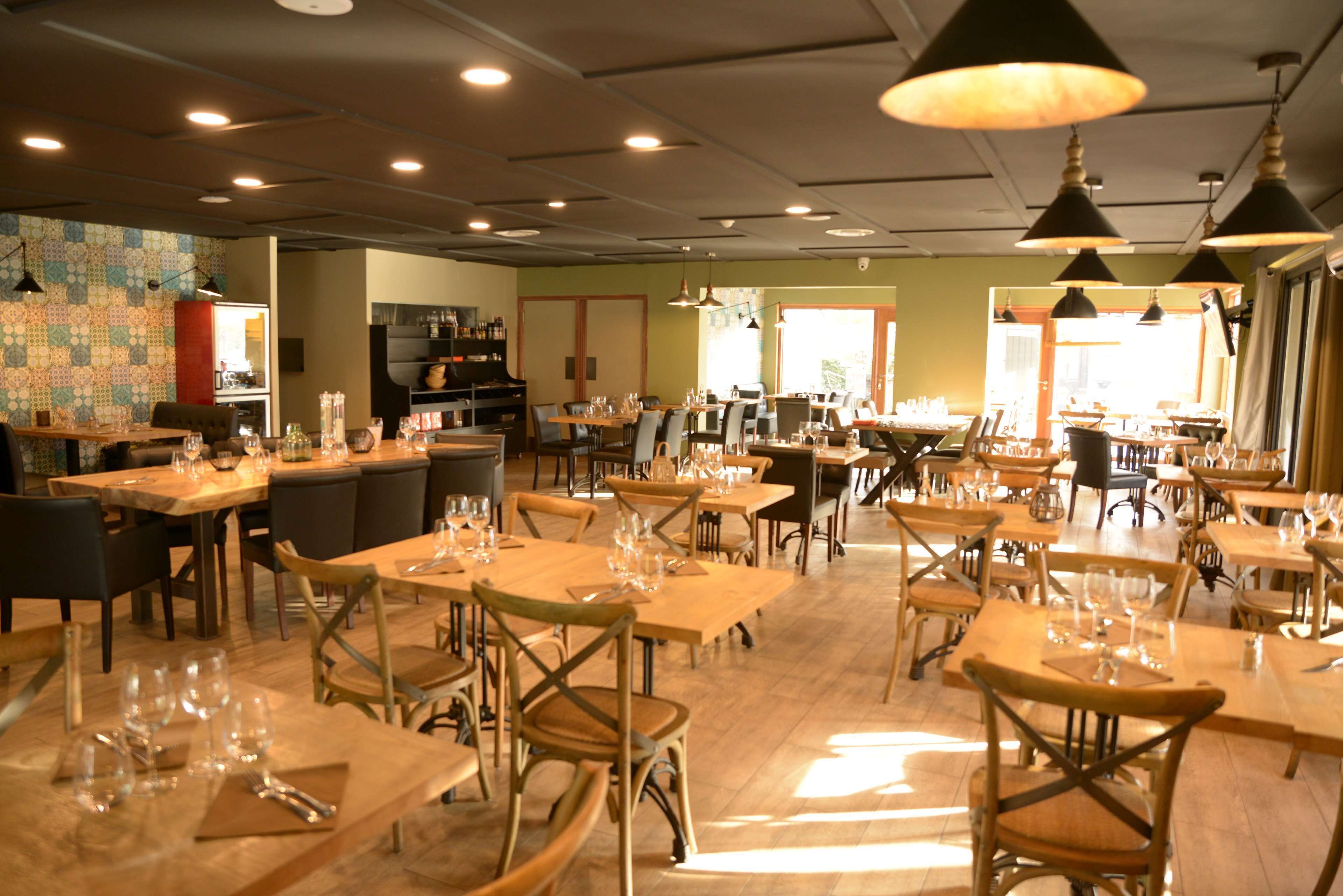 Ein großzügiges Restaurant mit mehreren Tischen und Stühlen, gut beleuchtet mit Pendelleuchten und einer gemütlichen Atmosphäre.