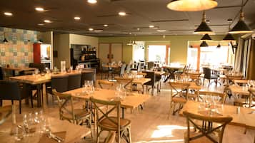 Ein großzügiges Restaurant mit mehreren Tischen und Stühlen, gut beleuchtet mit Pendelleuchten und einer gemütlichen Atmosphäre.