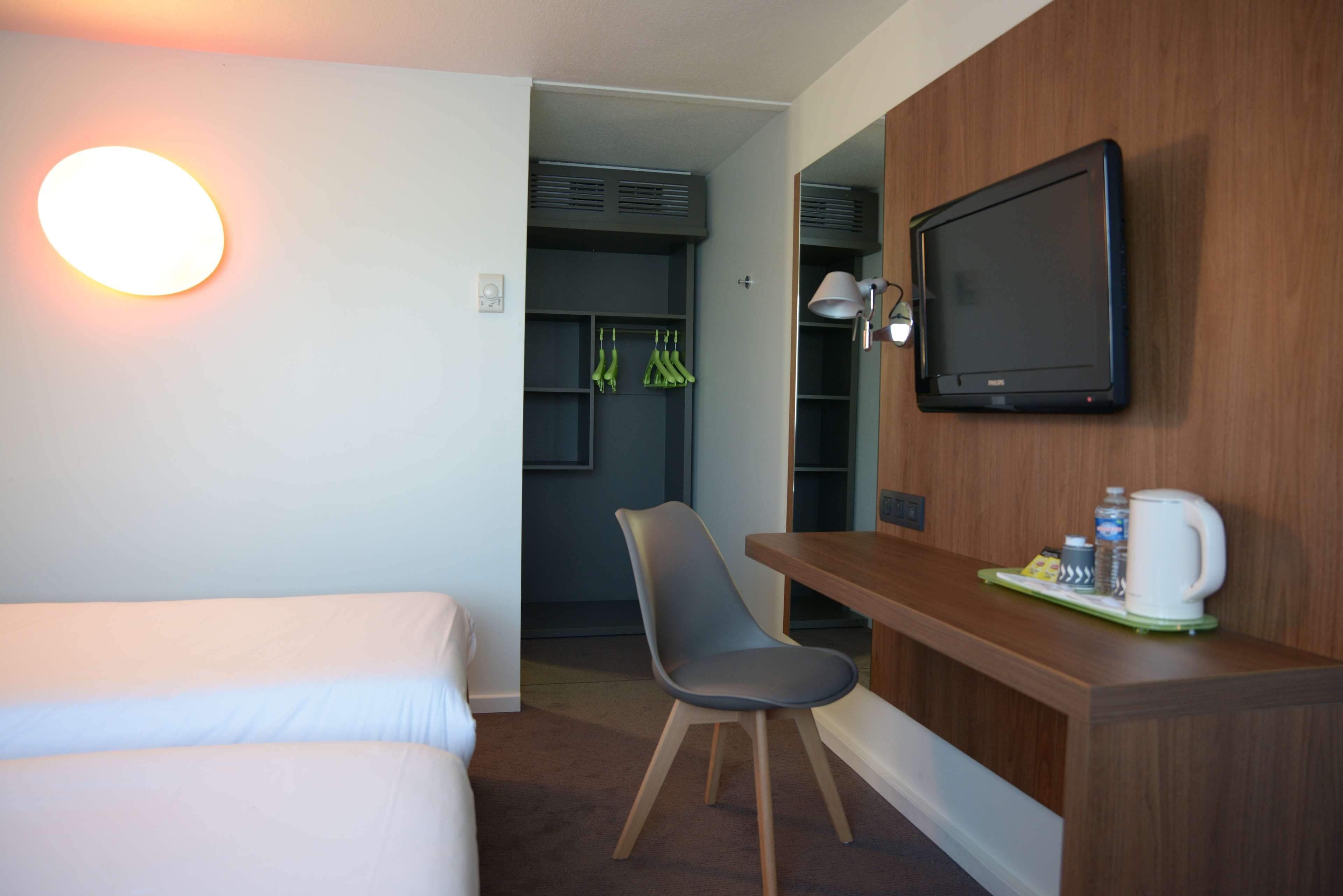 Una habitación de hotel con cama, escritorio con silla, televisor y cafetera.