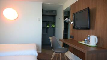 Una habitación de hotel con cama, escritorio con silla, televisor y cafetera.