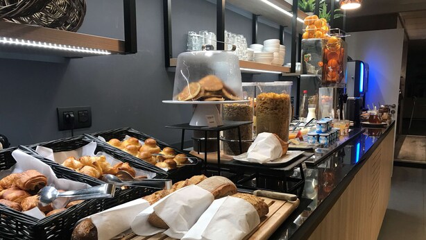Un espace buffet proposant une variété de produits de boulangerie, notamment des croissants et du pain, ainsi qu’un assortiment de boissons et de condiments.