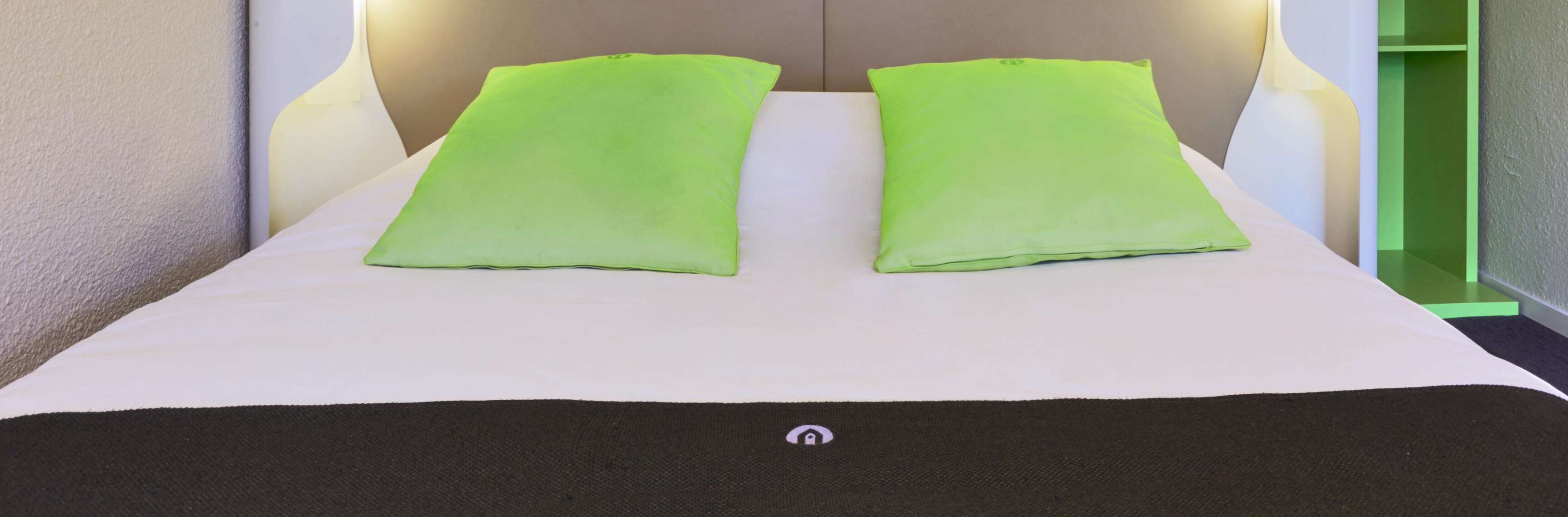 Una cama con dos almohadas, una colcha negra y un cabecero con iluminación integrada.