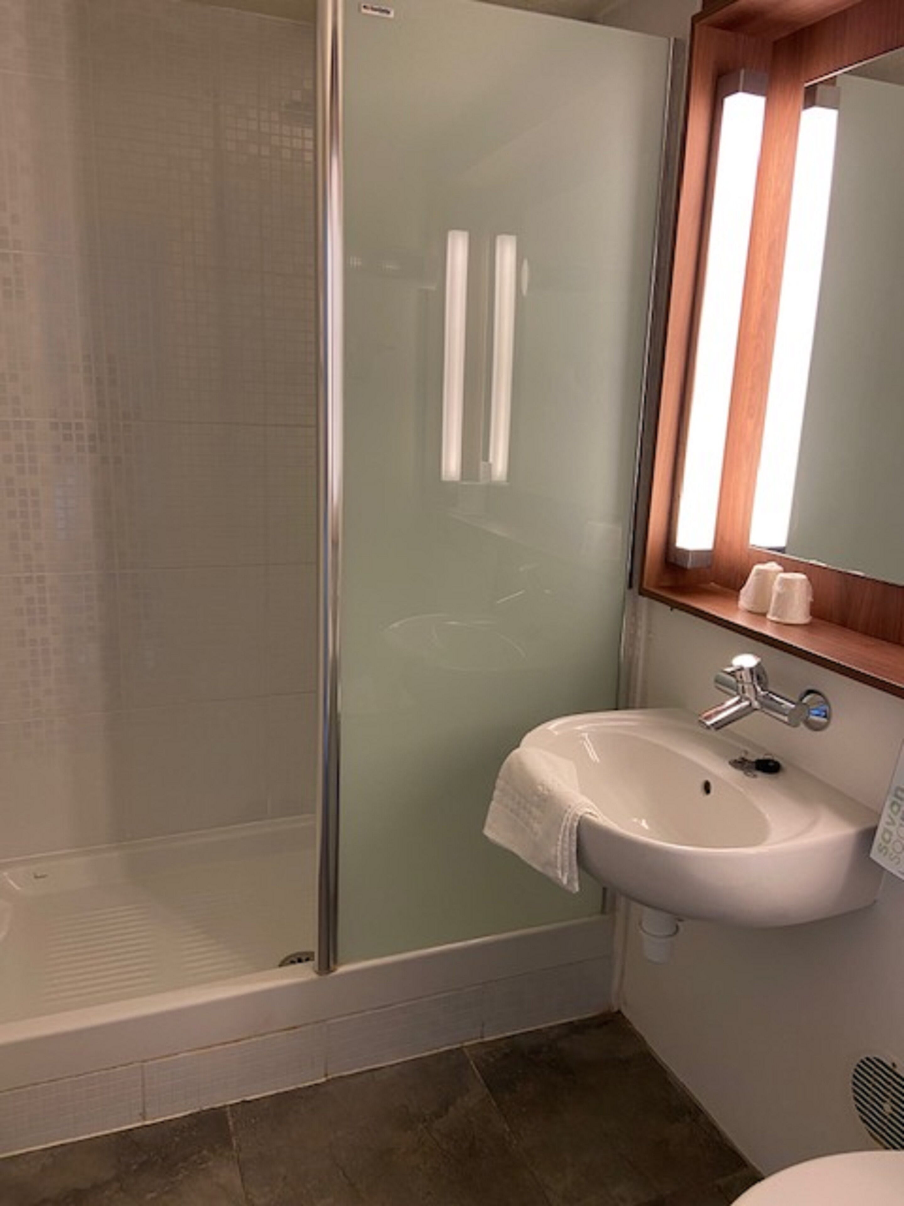 Ein Badezimmer mit Duschkabine aus Glas, einem weißen Waschbecken und einem Spiegel darüber sowie einer Holzauskleidung.
