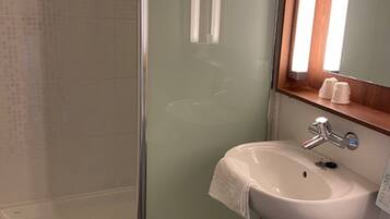 Un baño con cabina de ducha de vidrio, un lavamanos blanco con espejo y encimera de madera.