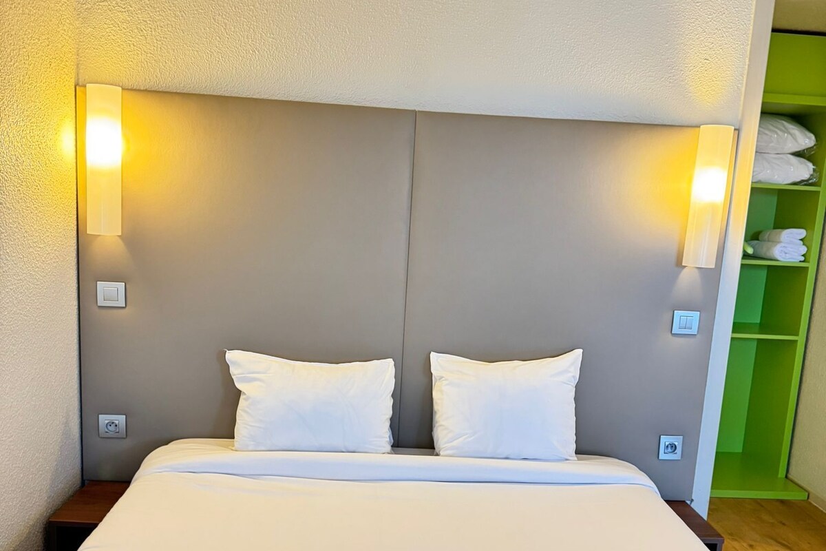 Quarto de hotel com uma cama grande, duas luminárias de cabeceira e um móvel de armazenamento verde.